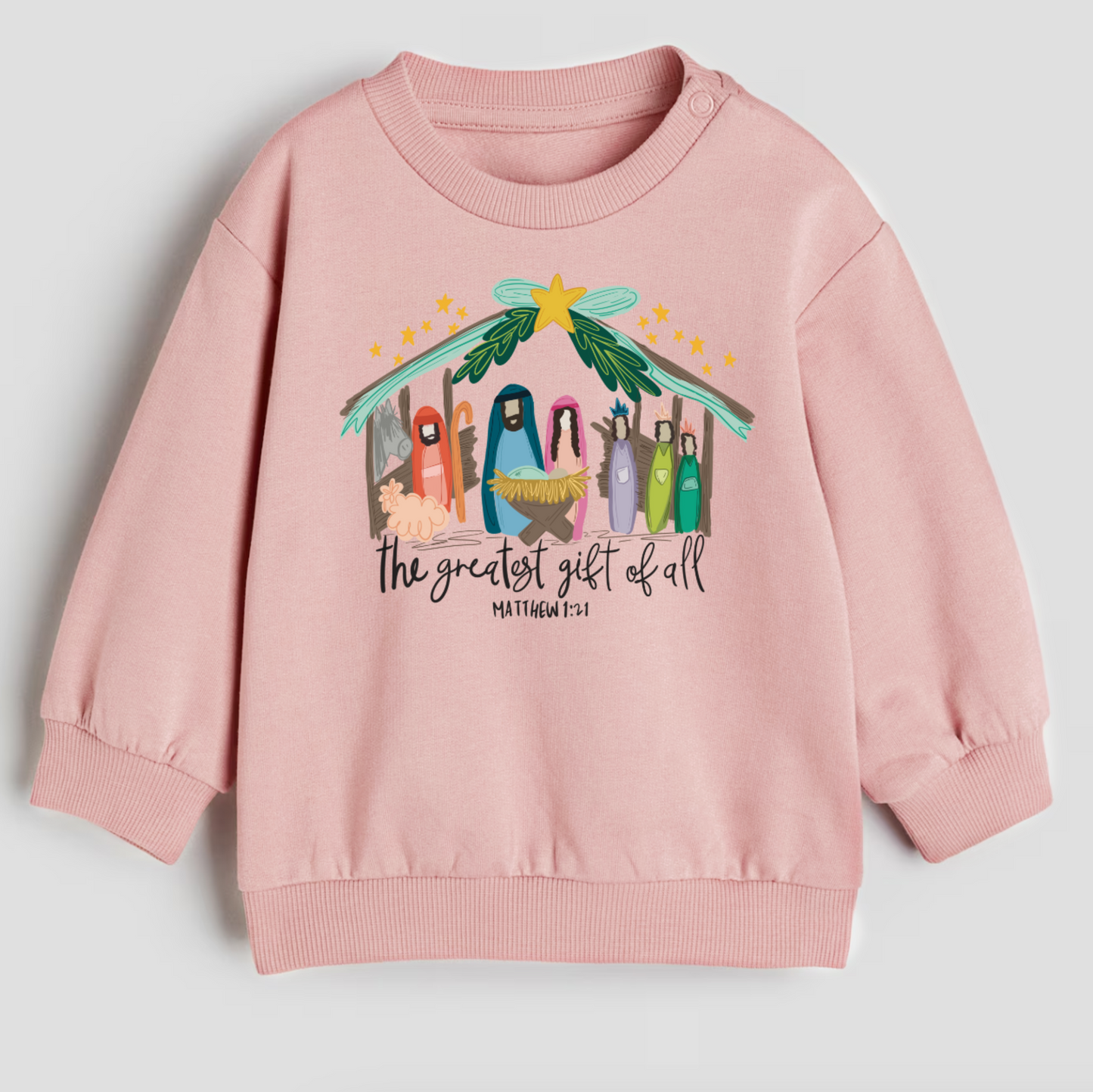 Pink sweatshirt with nativity scene design and text on a light gray background