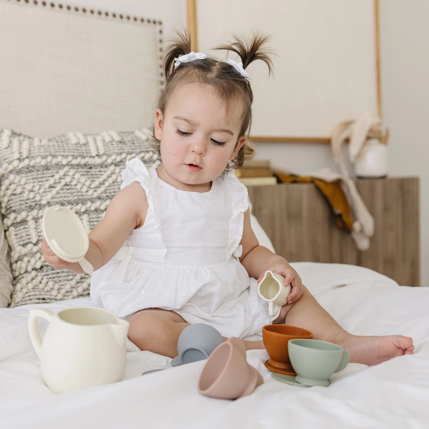 Child playing with silicone tea set toys on a bed in a bedroom setting