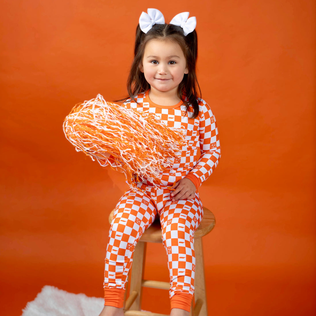 Kids wearing orange and white checkerboard bamboo two piece pajamas ready for game day