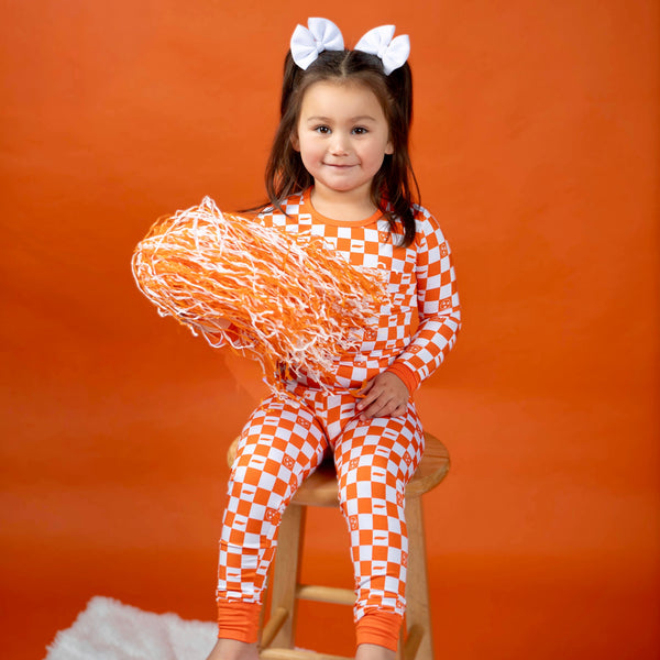 Kids wearing orange and white checkerboard bamboo two piece pajamas ready for game day
