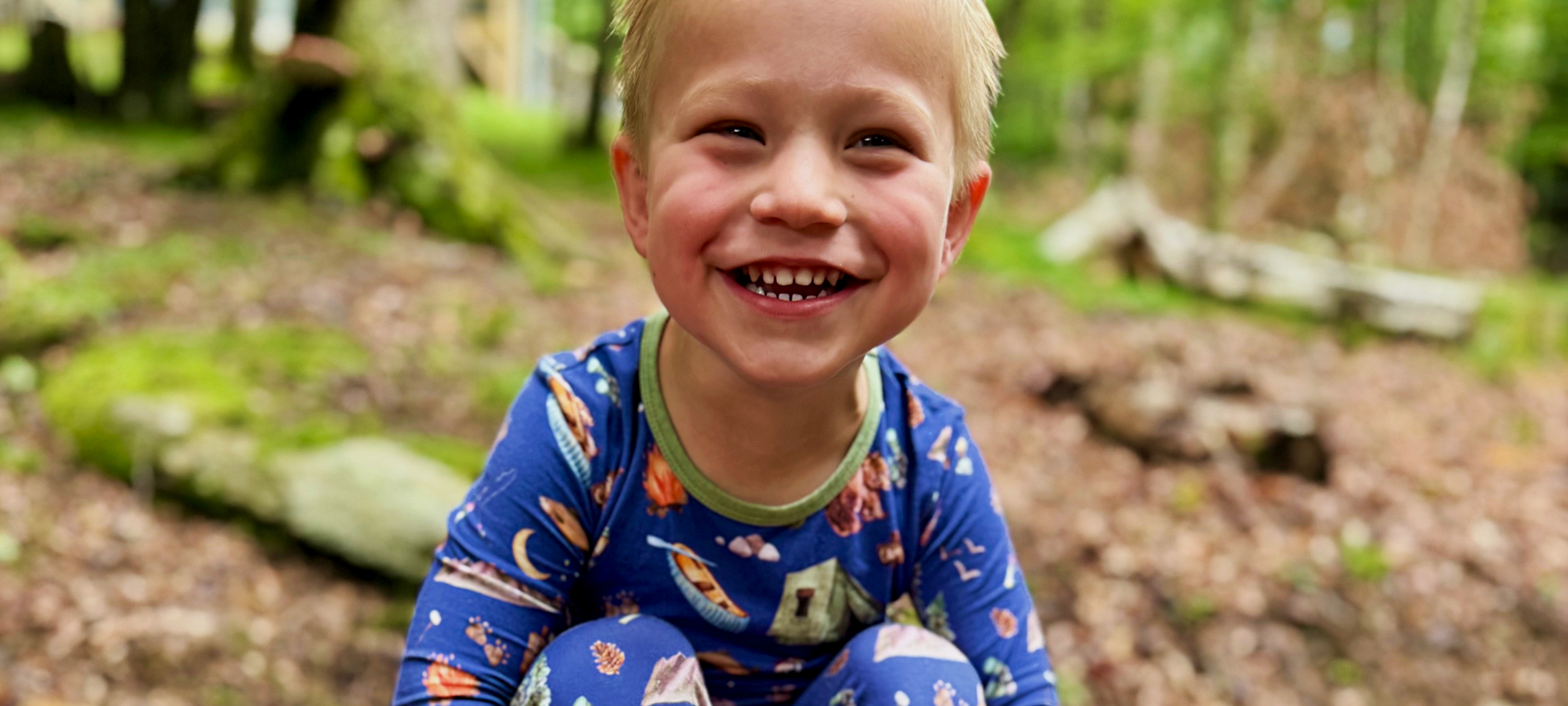 Child in a forest wearing a blue Great smoky mountains bamboo pajamas with animal prints.
