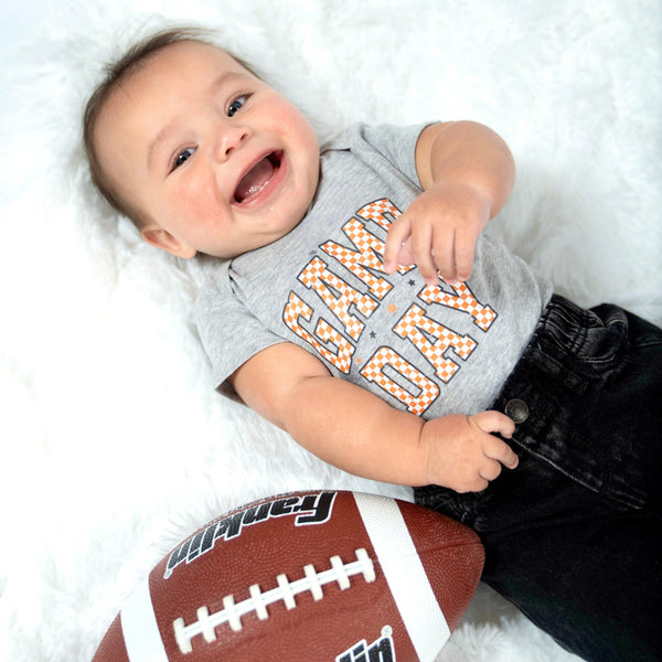 Baby lying on a white surface with a game day checkerboard tennessee shirt with a Franklin football