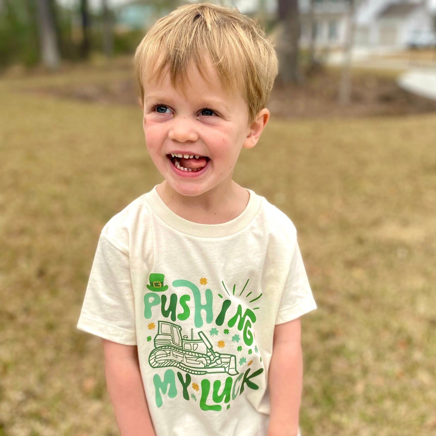 Child wearing a white t-shirt with pushing my luck green text and graphics outdoors