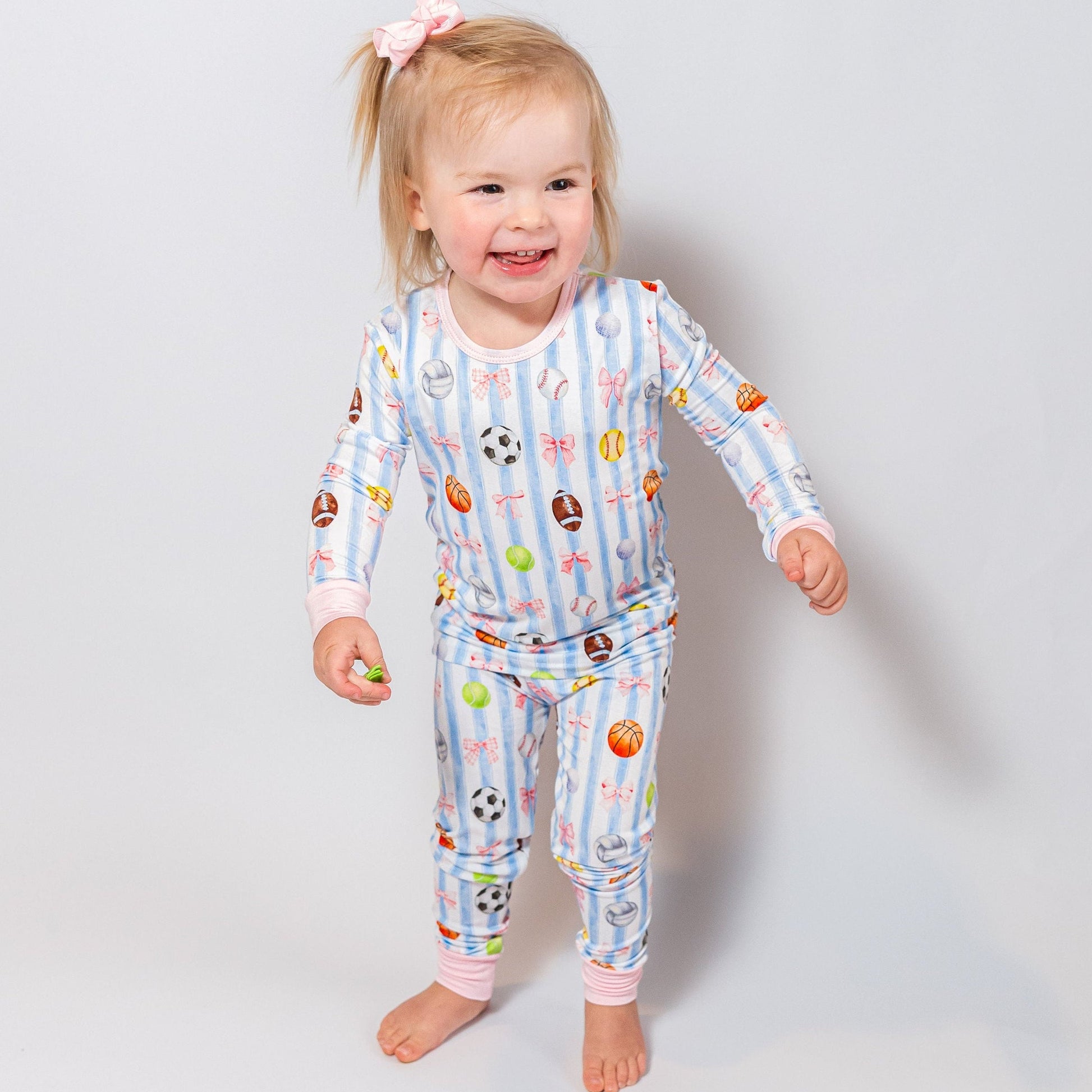 Child wearing a colorful sports and bows pajama set with various patterns on a plain background