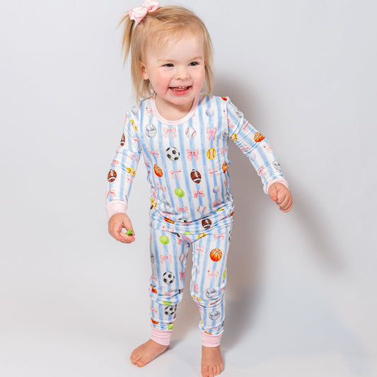 Child wearing a colorful sports and bows pajama set with various patterns on a plain background
