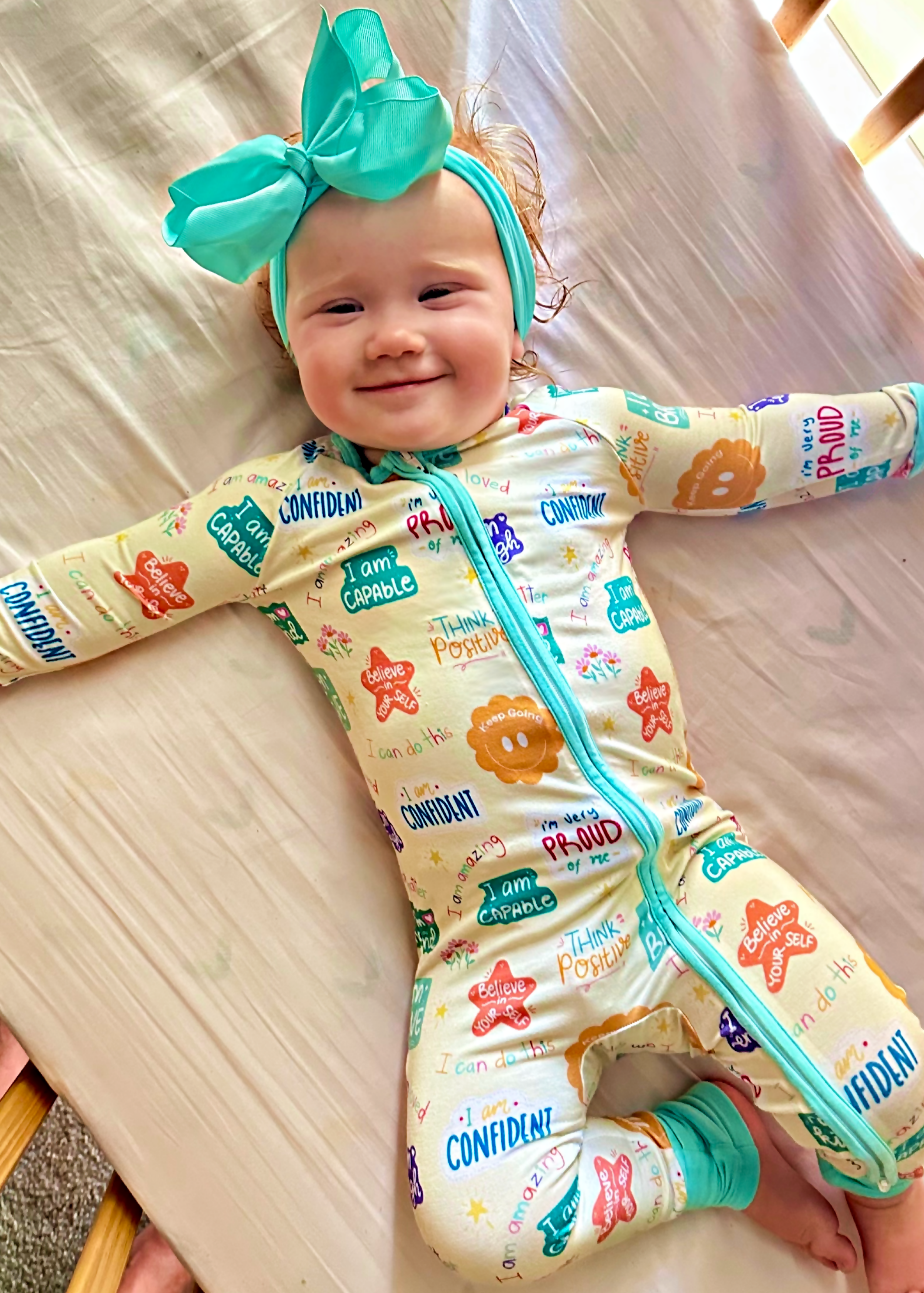Baby in a colorful outfit with a teal headband lying on a bed.