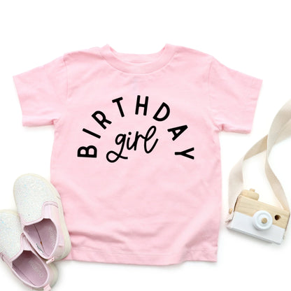 Pink t-shirt with 'Birthday girl' text, white shoes, and a small camera on a white background