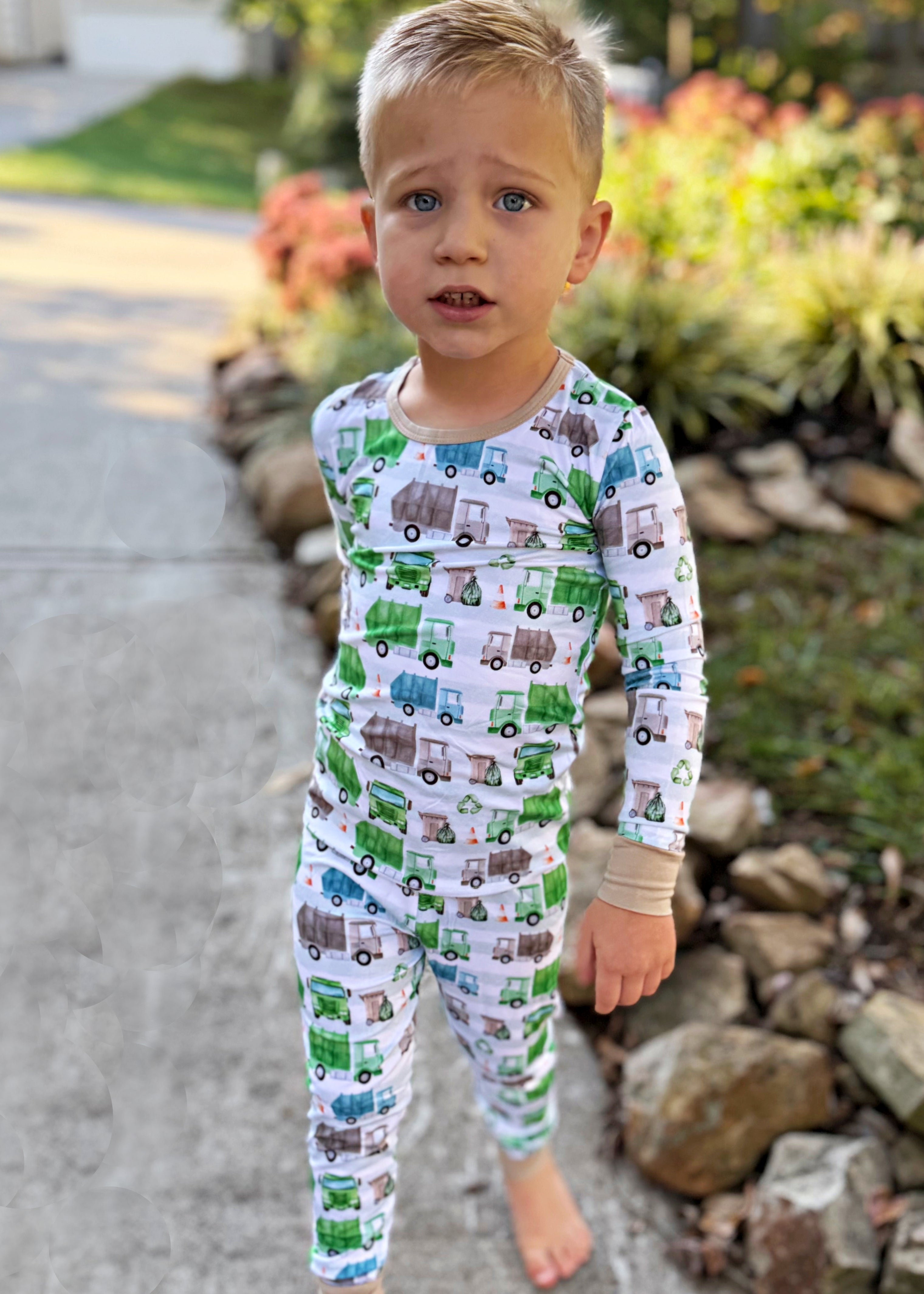 Child wearing pajamas with truck pattern standing outdoors.