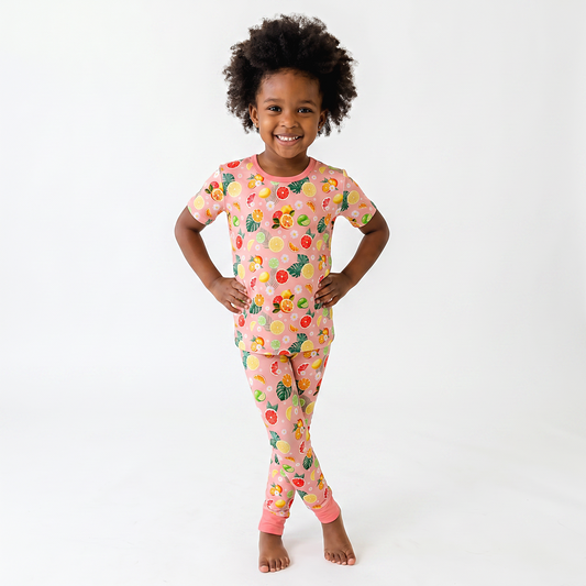 Child wearing a colorful citrus pajama set with a fruit pattern on a white background