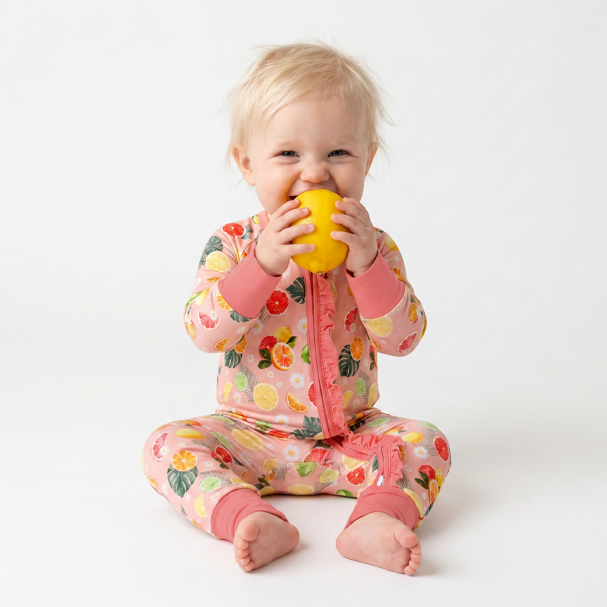 Child wearing a colorful citrus onesie holding a lemon on a white background