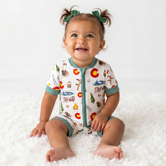 Baby wearing a colorado patterned onesie sitting on a white surface