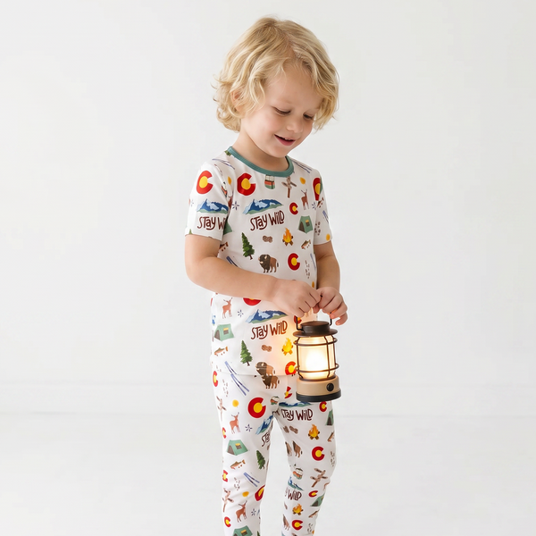 Child wearing pajamas with nature-themed print, holding a lantern on a plain background