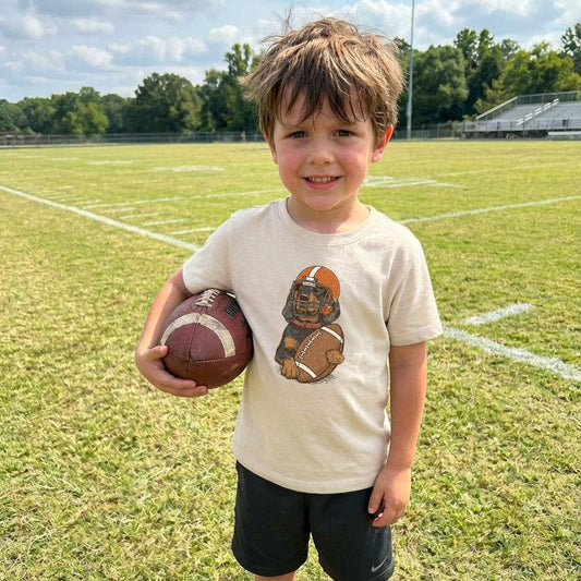 Child holding a football on a sports field with a clear sky