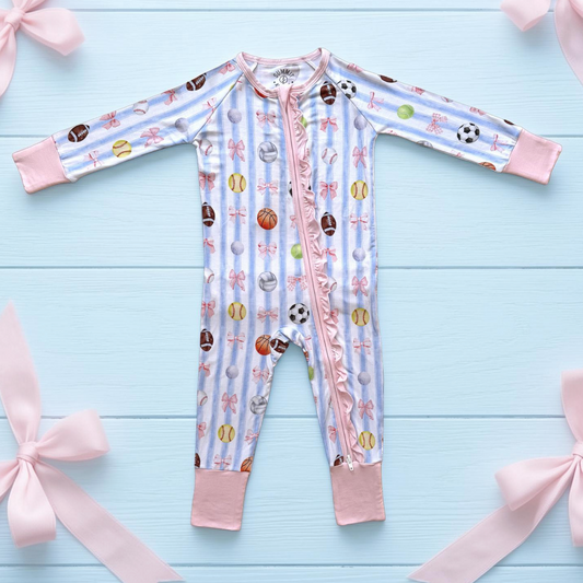 Baby onesie with sports-themed print on a light blue wooden surface with pink bows.