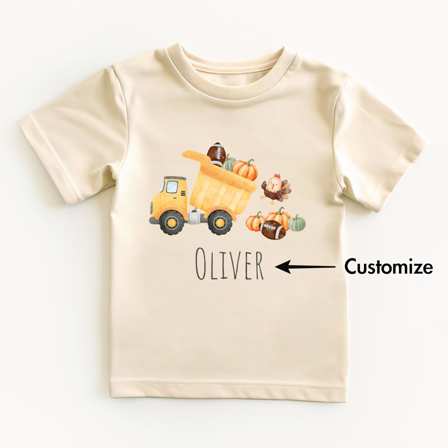 Beige t-shirt with a cartoon dump truck, pumpkins, and a turkey on a white background.