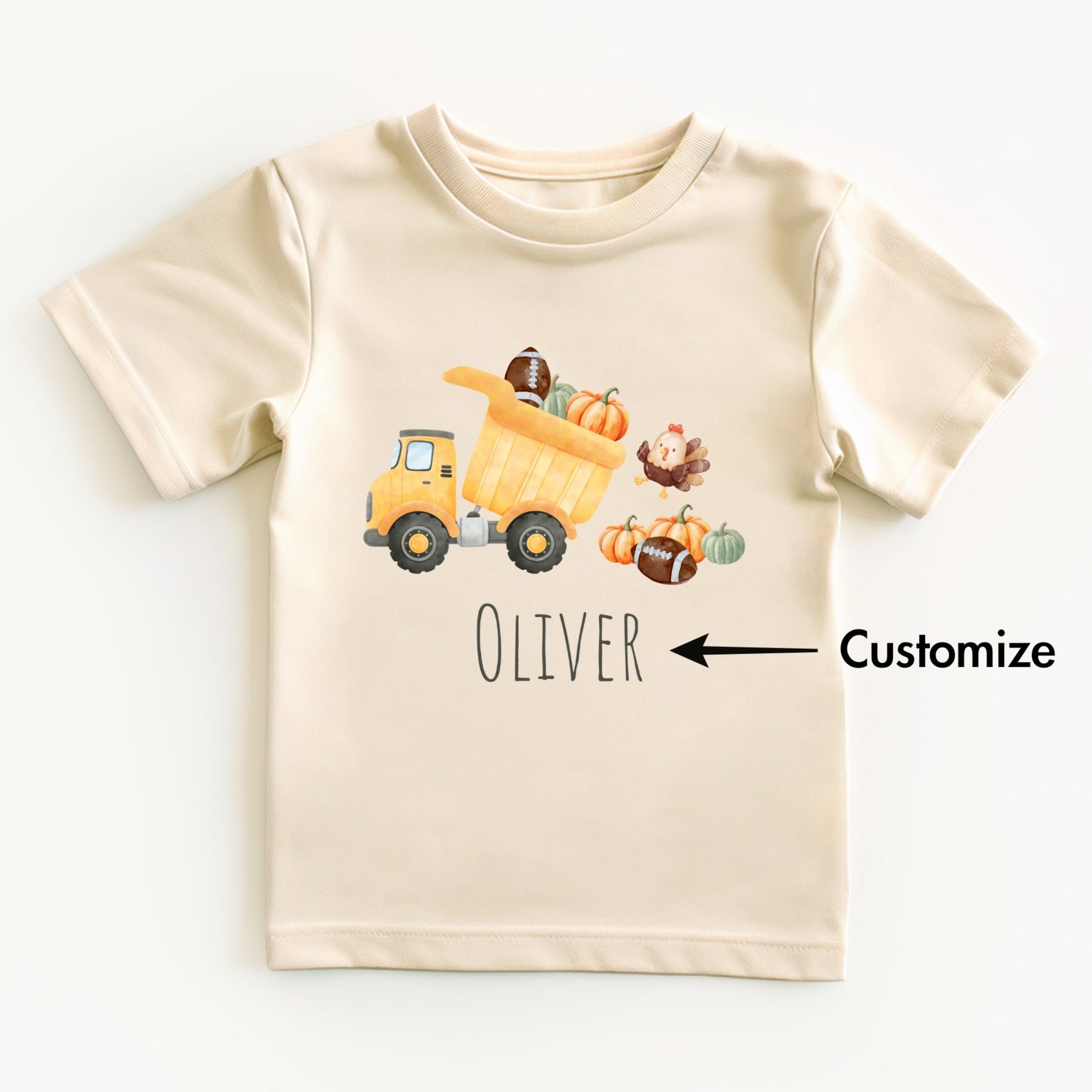 Beige t-shirt with a cartoon dump truck, pumpkins, and a turkey on a white background.