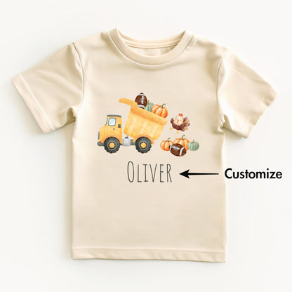 Beige t-shirt with a cartoon dump truck, pumpkins, and a turkey on a white background.