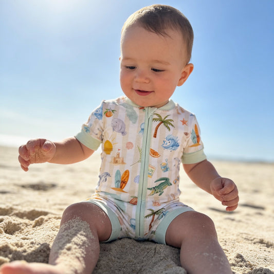Baby sitting on the sand wearing a Florida romper with sea-themed design.