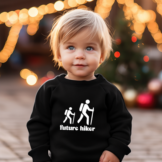Child wearing a black sweatshirt with 'future hiker' text and hiking icons, Christmas lights and tree in the background.