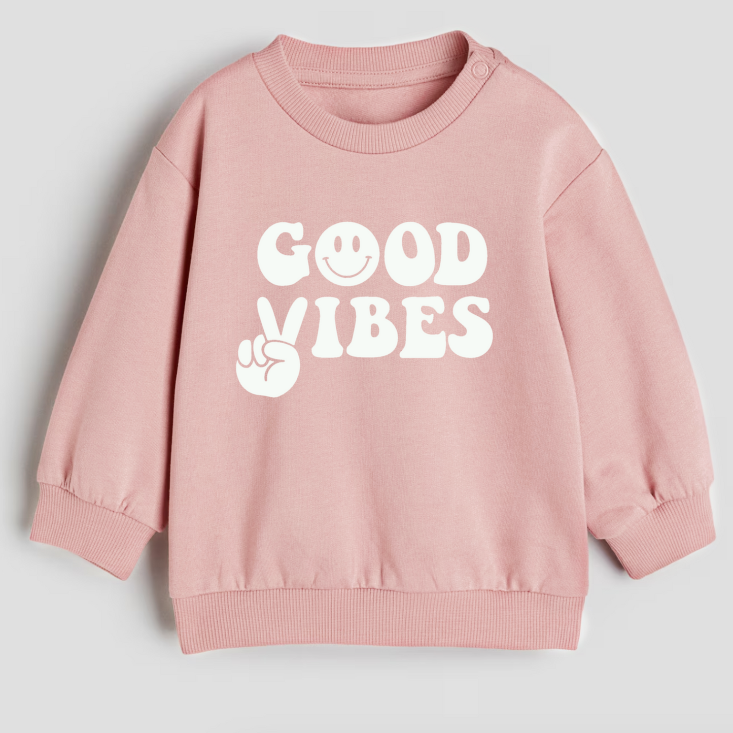 Pink sweatshirt with 'Good Vibes' text on a light gray background