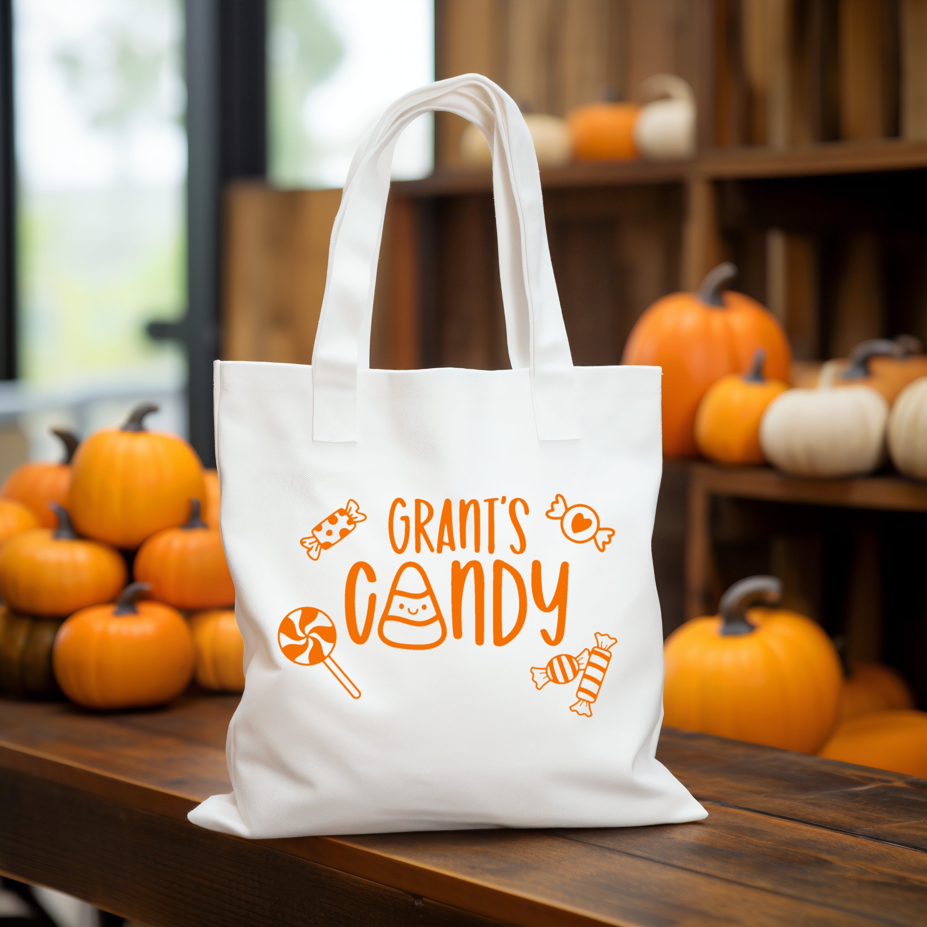 White tote bag with 'GRANT'S CANDY' text on a wooden table with pumpkins in the background