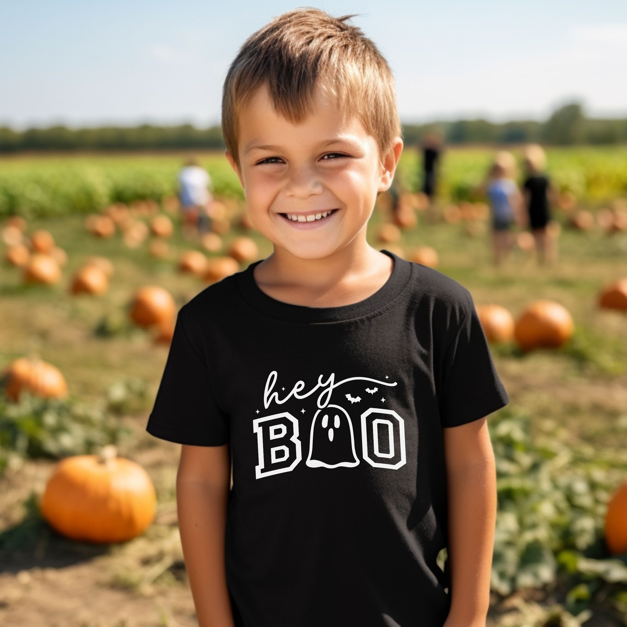 Child wearing a black t-shirt with 'hey BOO' text in a pumpkin patch