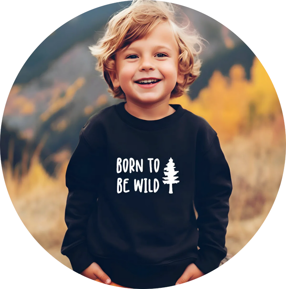 Child wearing a black sweatshirt with 'Born to Be Wild' text and tree graphic, standing in front of a blurred natural background.