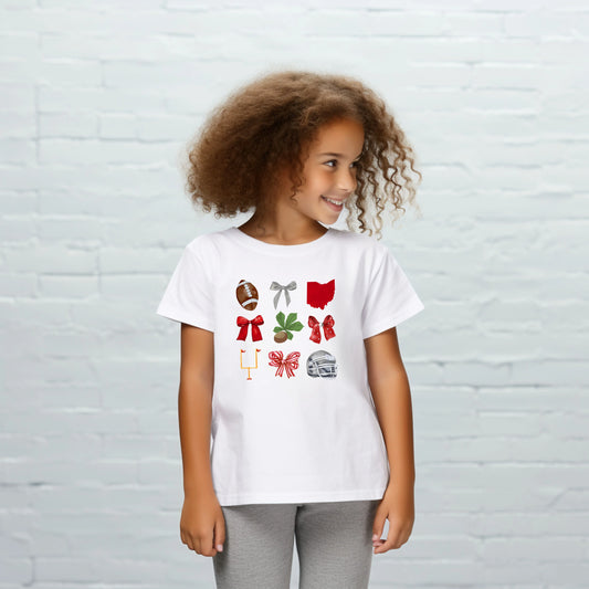 Child wearing a white t-shirt with colorful graphics against a light gray brick wall.