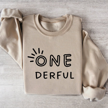 Beige sweatshirt with 'ONE DERFUL' text on a wooden surface