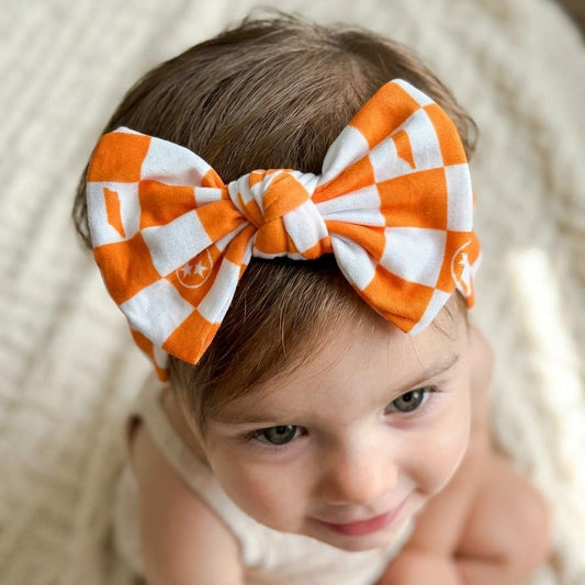 Child wearing an orange and white checkered bow headband on a neutral background