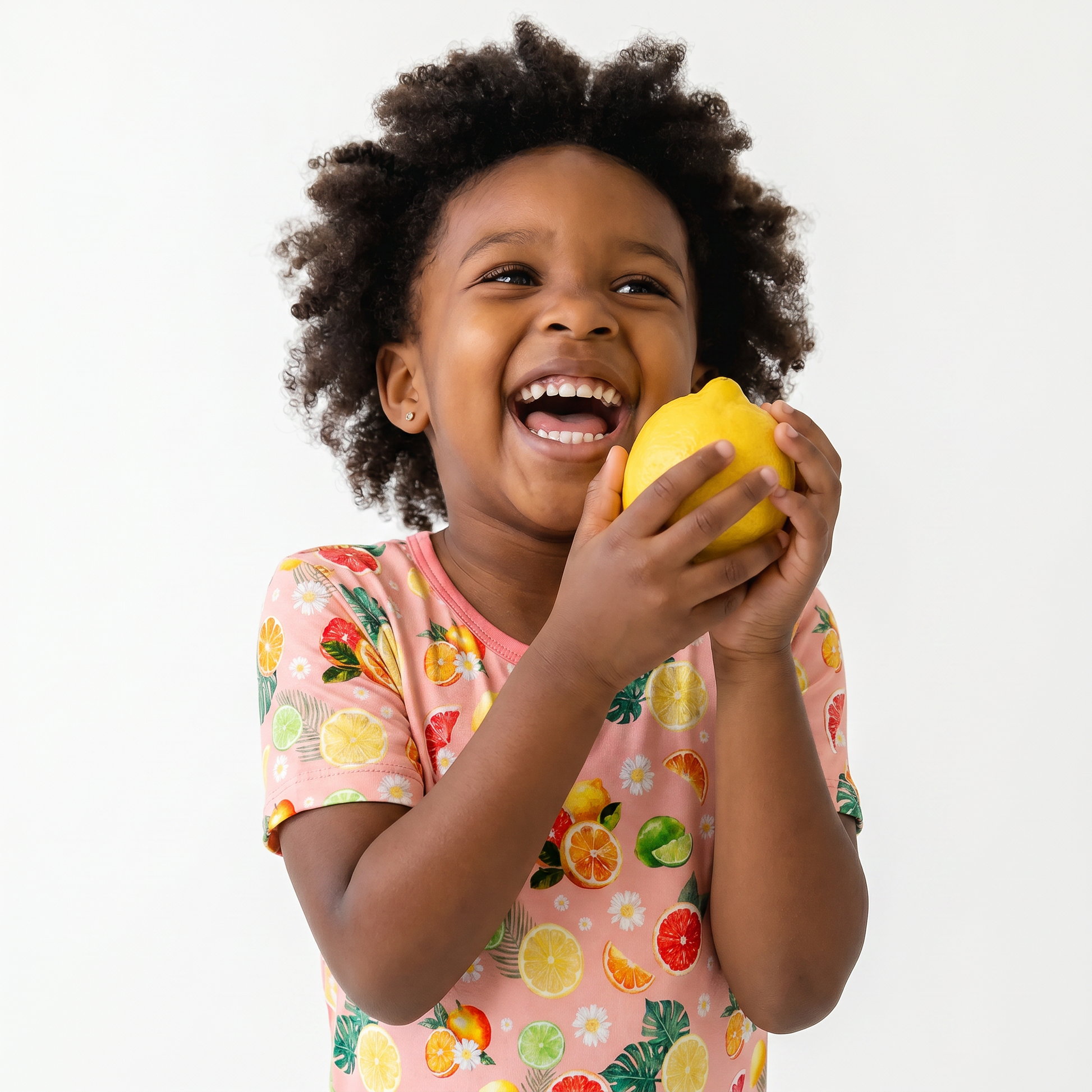 Child holding a lemon  in citrus pajamas with a white background