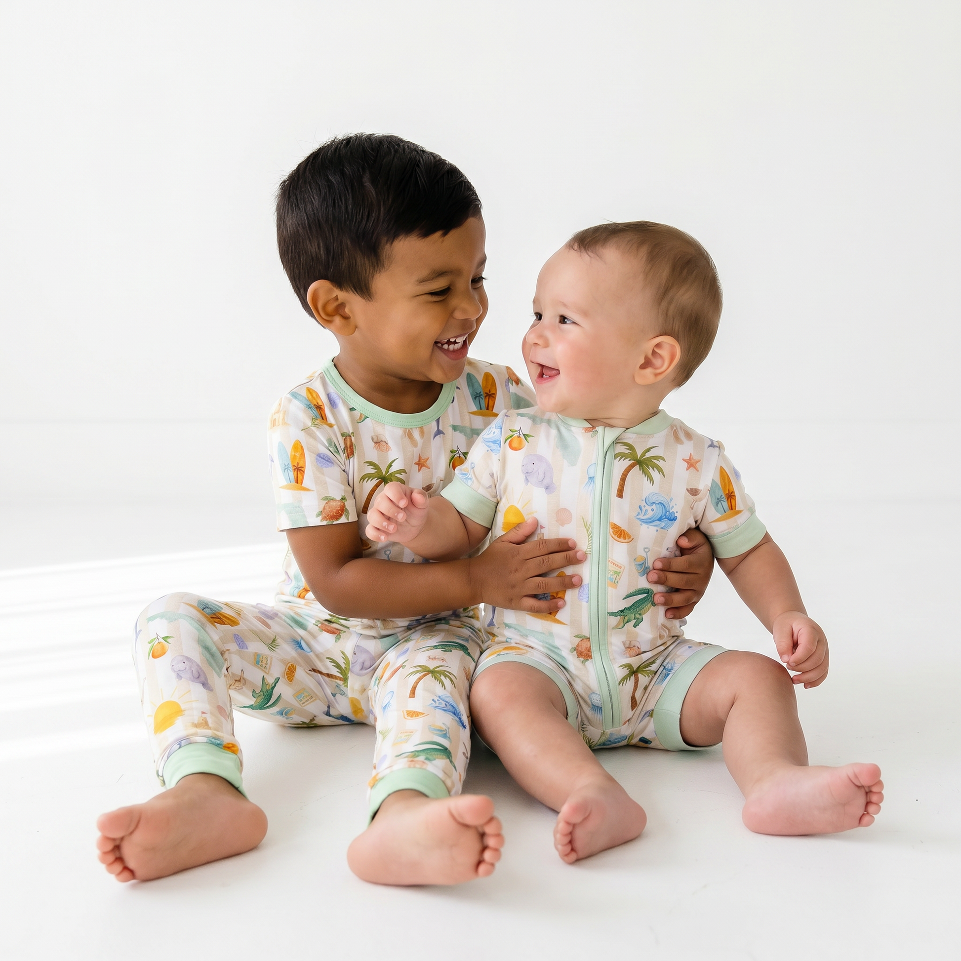 Two children wearing colorful Florida pajamas sitting on a white surface.