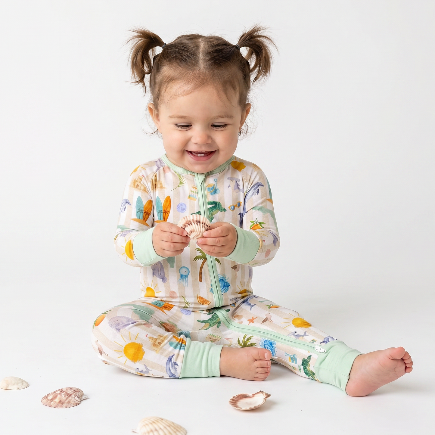 Child wearing a colorful pajama set with sea-themed design, sitting on a white background with seashells.