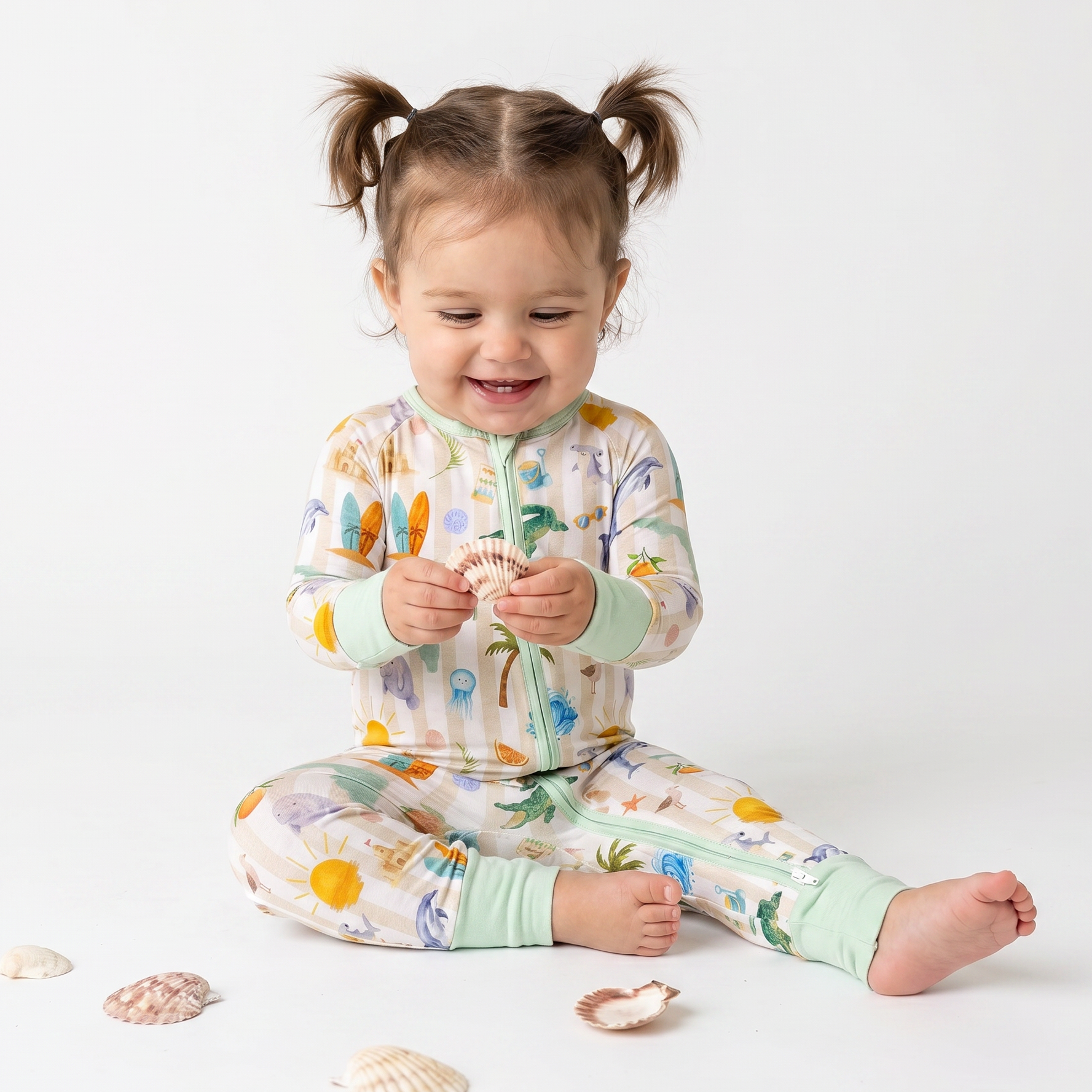 Child wearing a colorful pajama set with sea-themed design, sitting on a white background with seashells.