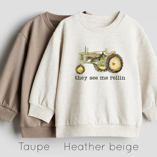 Two sweatshirts, one beige and one heather beige, with a tractor graphic and text on a light gray background.