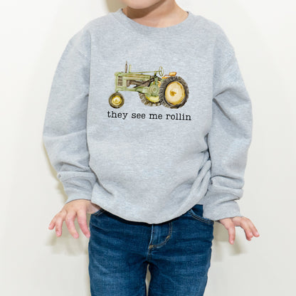 Child wearing a gray sweatshirt with a tractor graphic and text on a white background