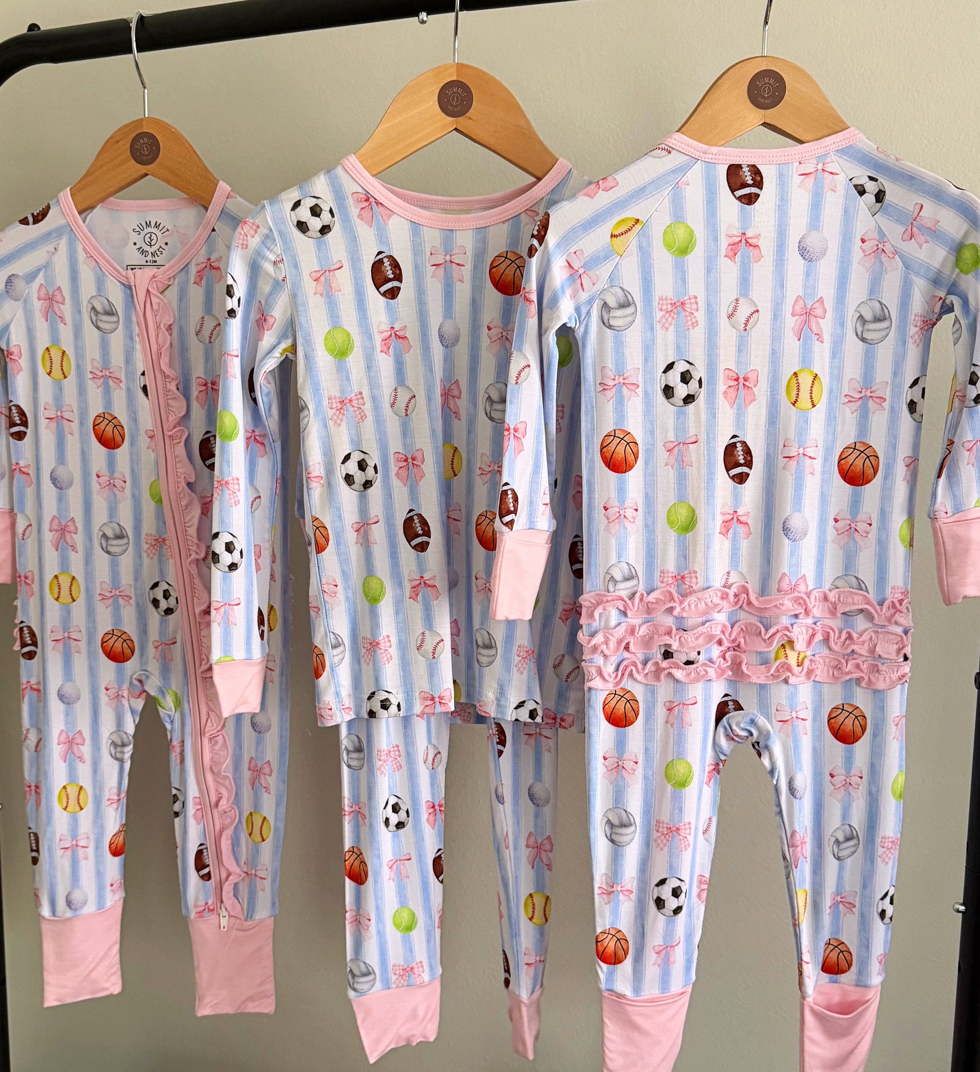 Three children's pajamas with sports patterns on hangers against a neutral background