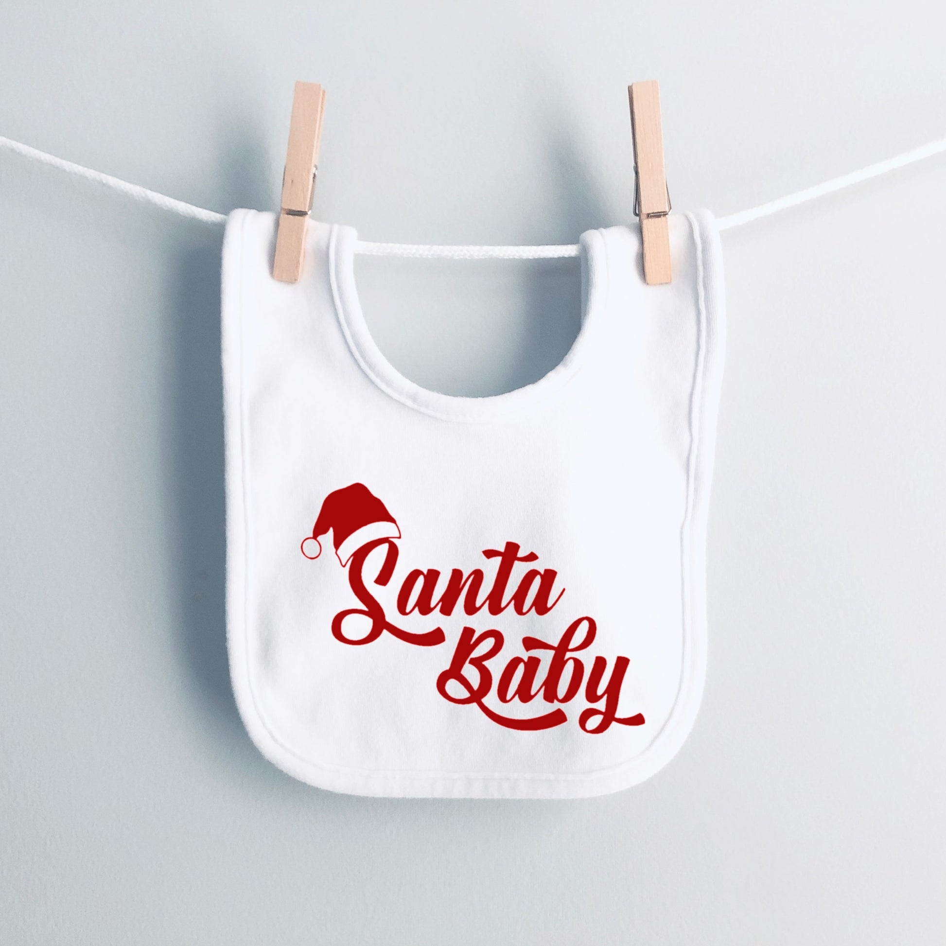 White bib with 'Santa Baby' text and Santa hat graphic hanging on a clothesline.