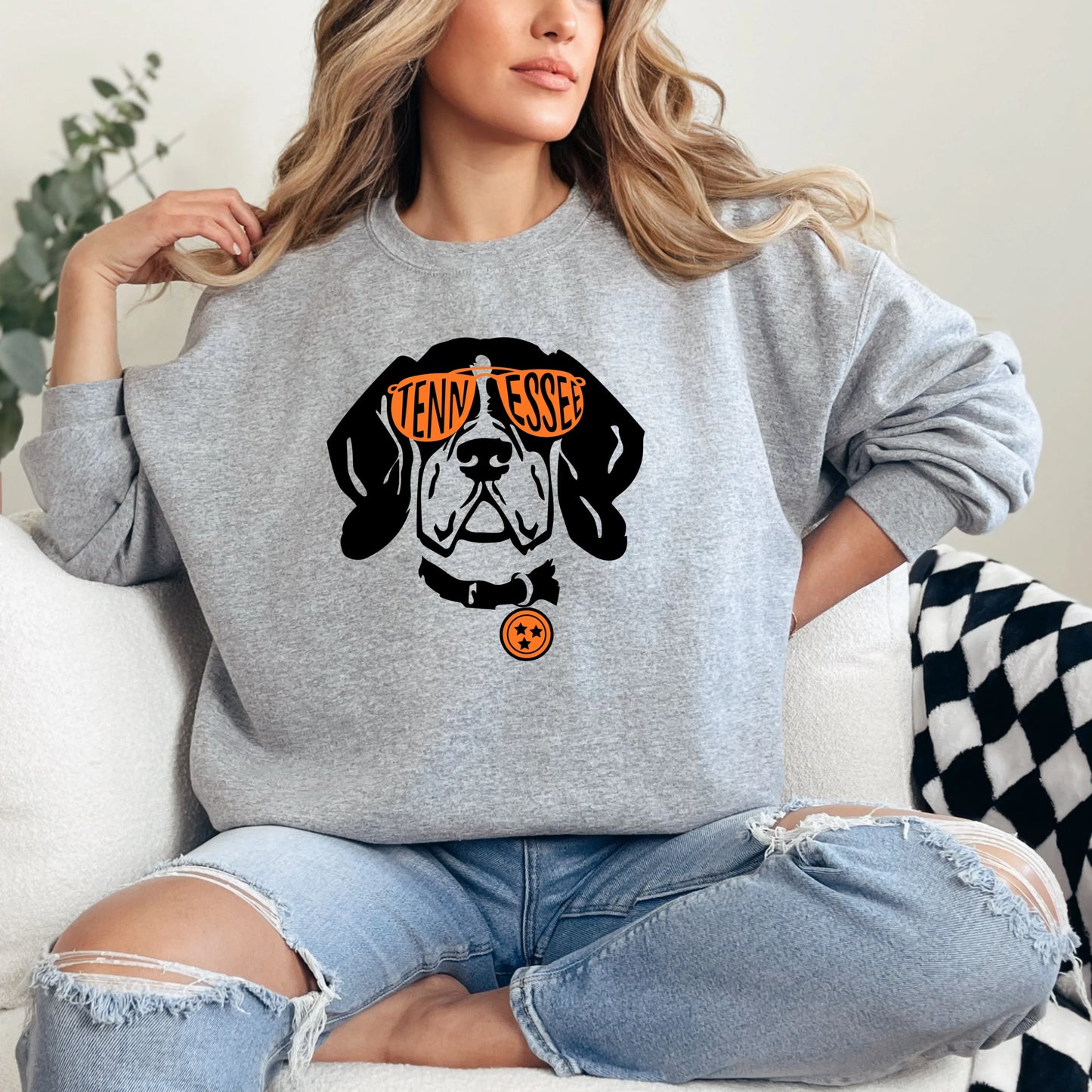 Person wearing a Vols gray sweatshirt with a dog graphic and text, sitting on a white couch.