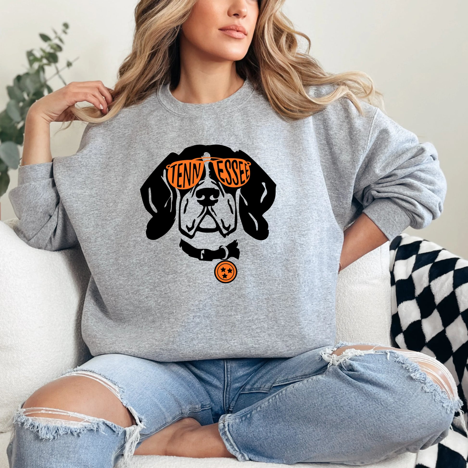 Person wearing a Vols gray sweatshirt with a dog graphic and text, sitting on a white couch.