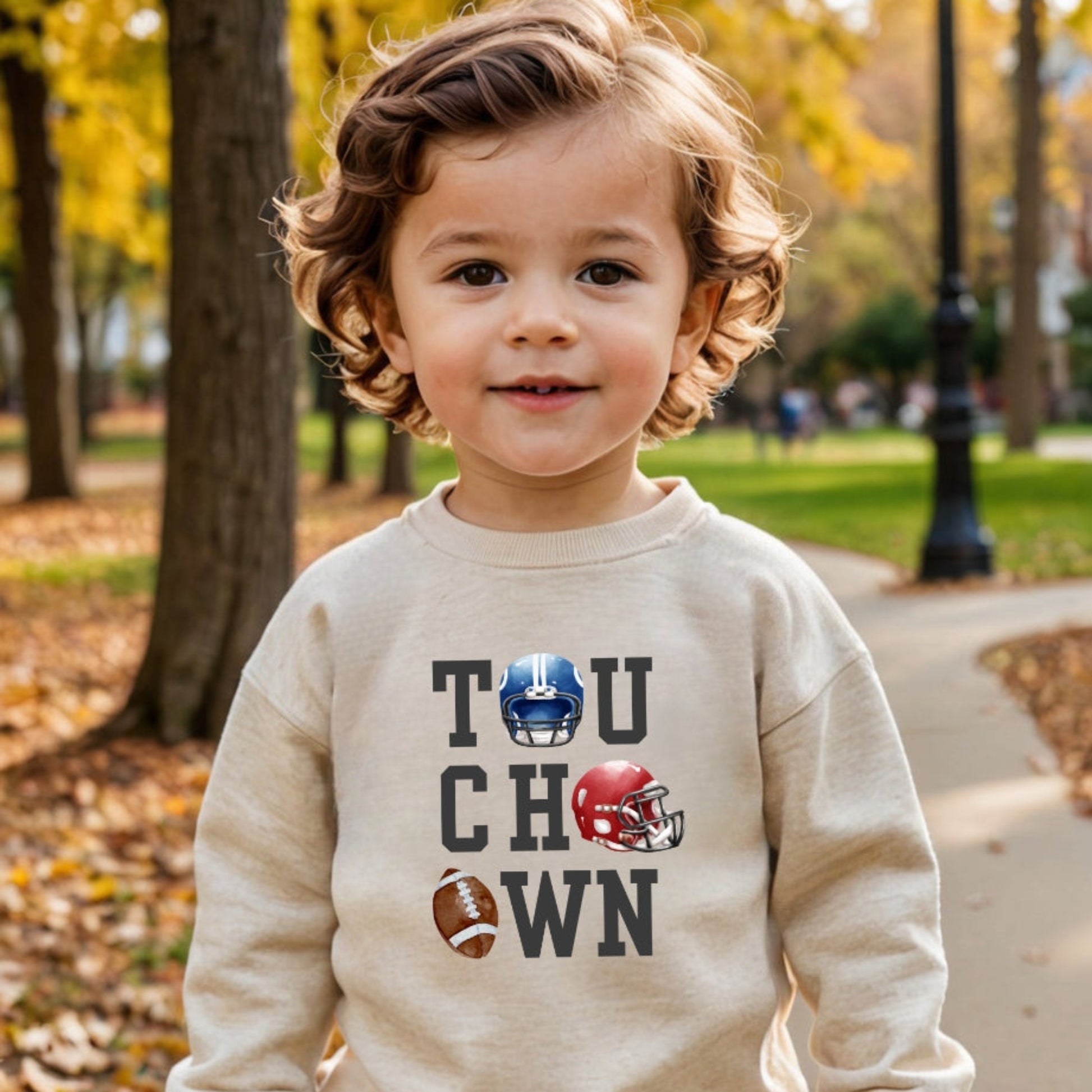 Child wearing a beige sweatshirt with 'Touchdown' text and football graphics in an outdoor setting.