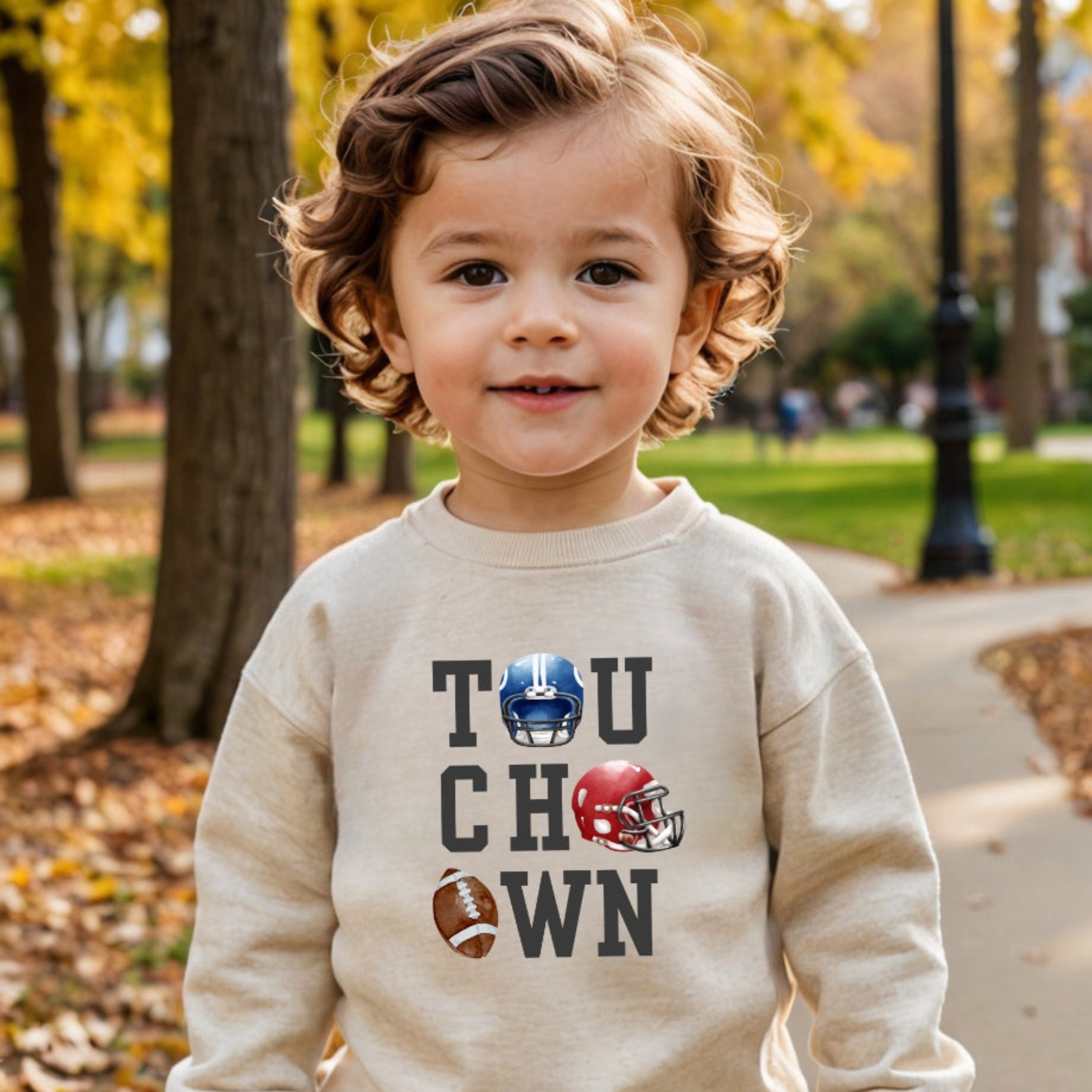 Child wearing a beige sweatshirt with 'Touchdown' text and football graphics in an outdoor setting.