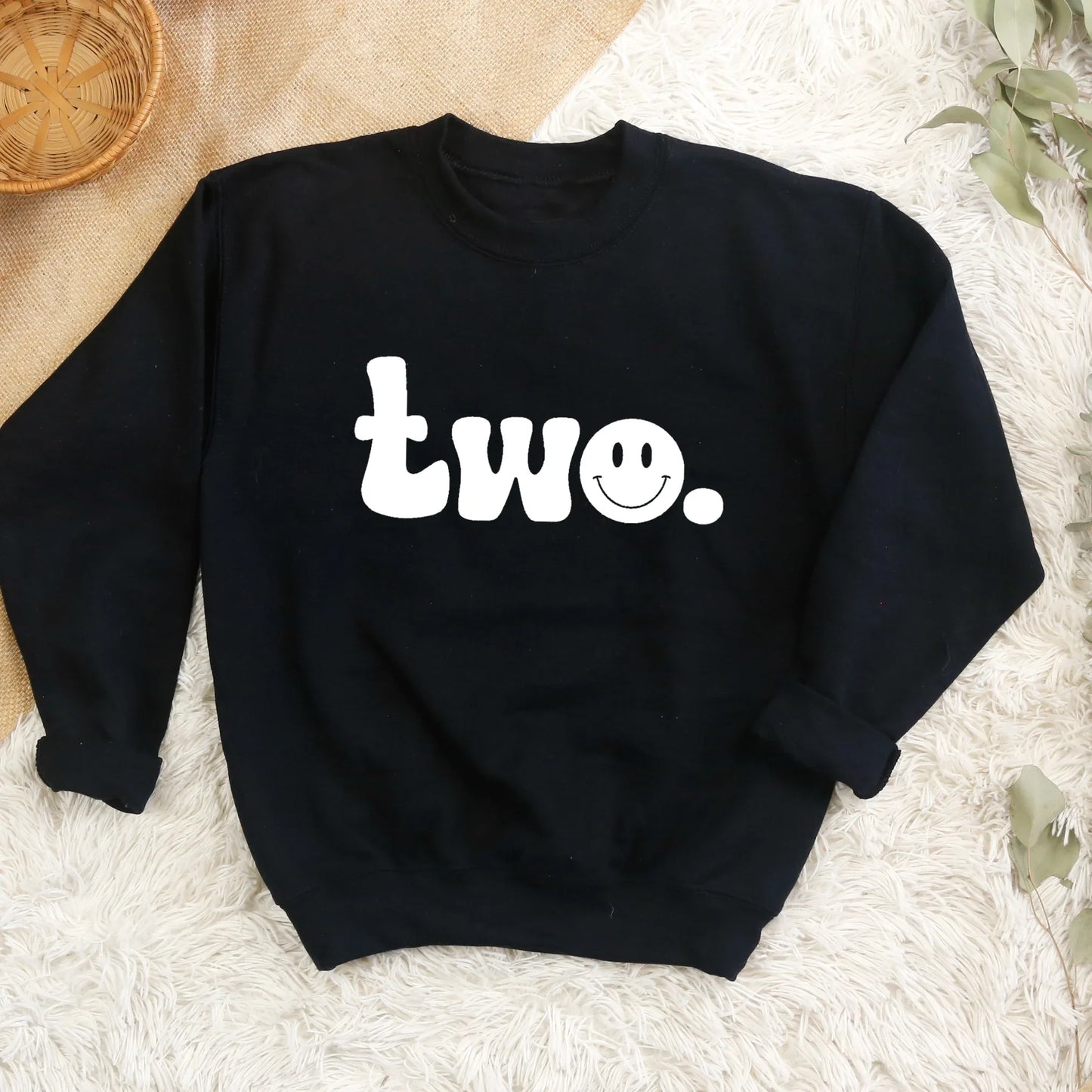 Black sweatshirt with 'two' printed on it, featuring a smiley face, on a textured surface.