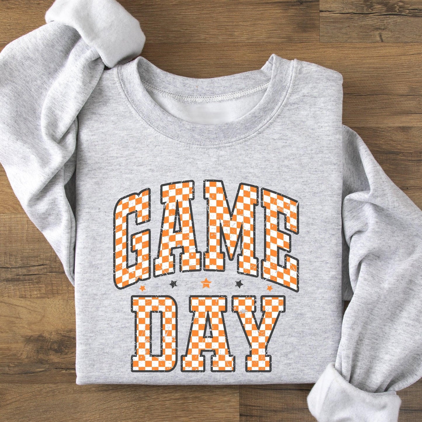 Gray sweatshirt with 'GAME DAY' text in orange checkered letters on a wooden surface